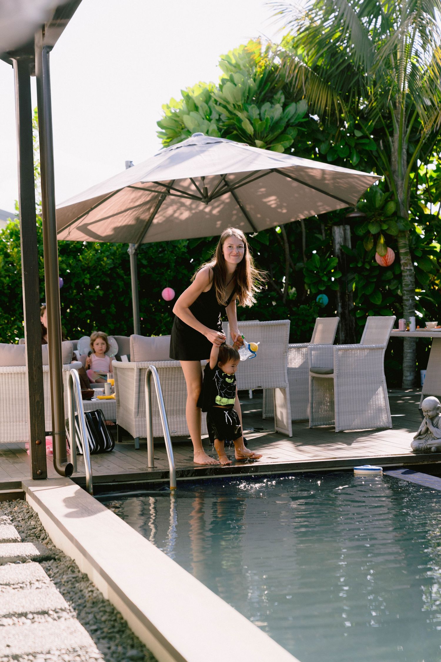 Pool party setting with umbrella and outdoor furniture surrounded by tropical landscaping.