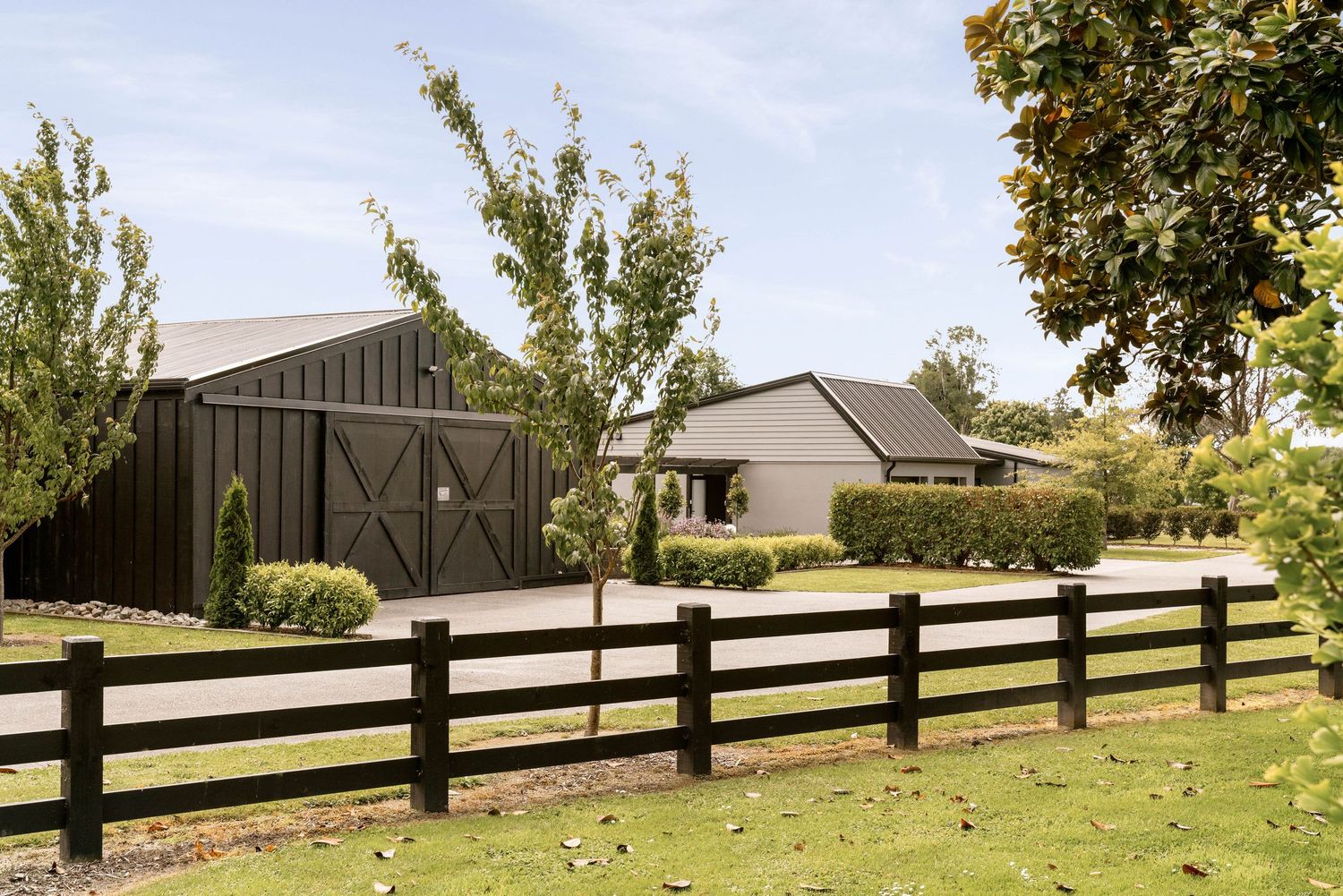 A rustic wooden fence stretches along the perimeter of a scenic residential property with trees in the background.