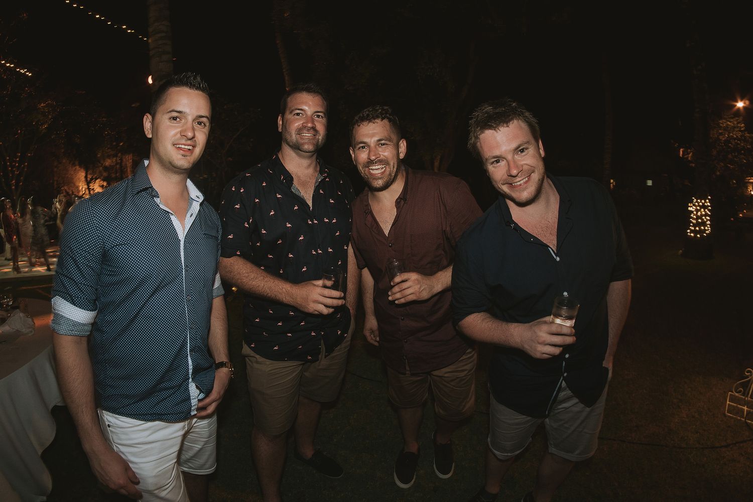 Four friends enjoy a nighttime celebration together in casual attire under outdoor lighting.