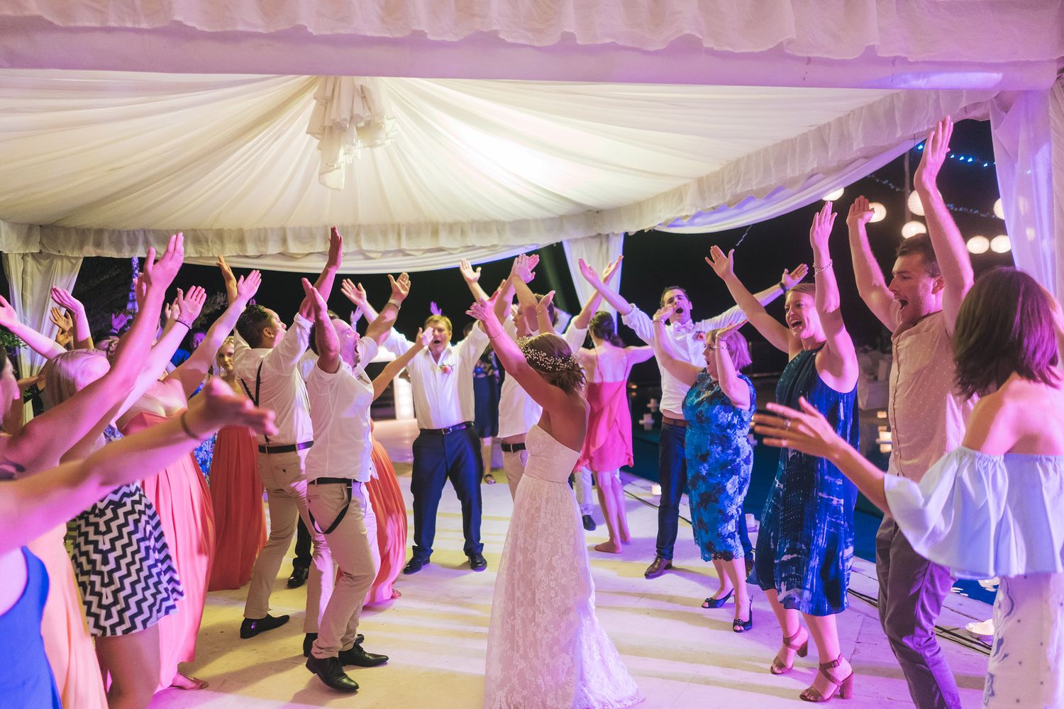 Wedding reception dance party with pink lighting under a white tent canopy.