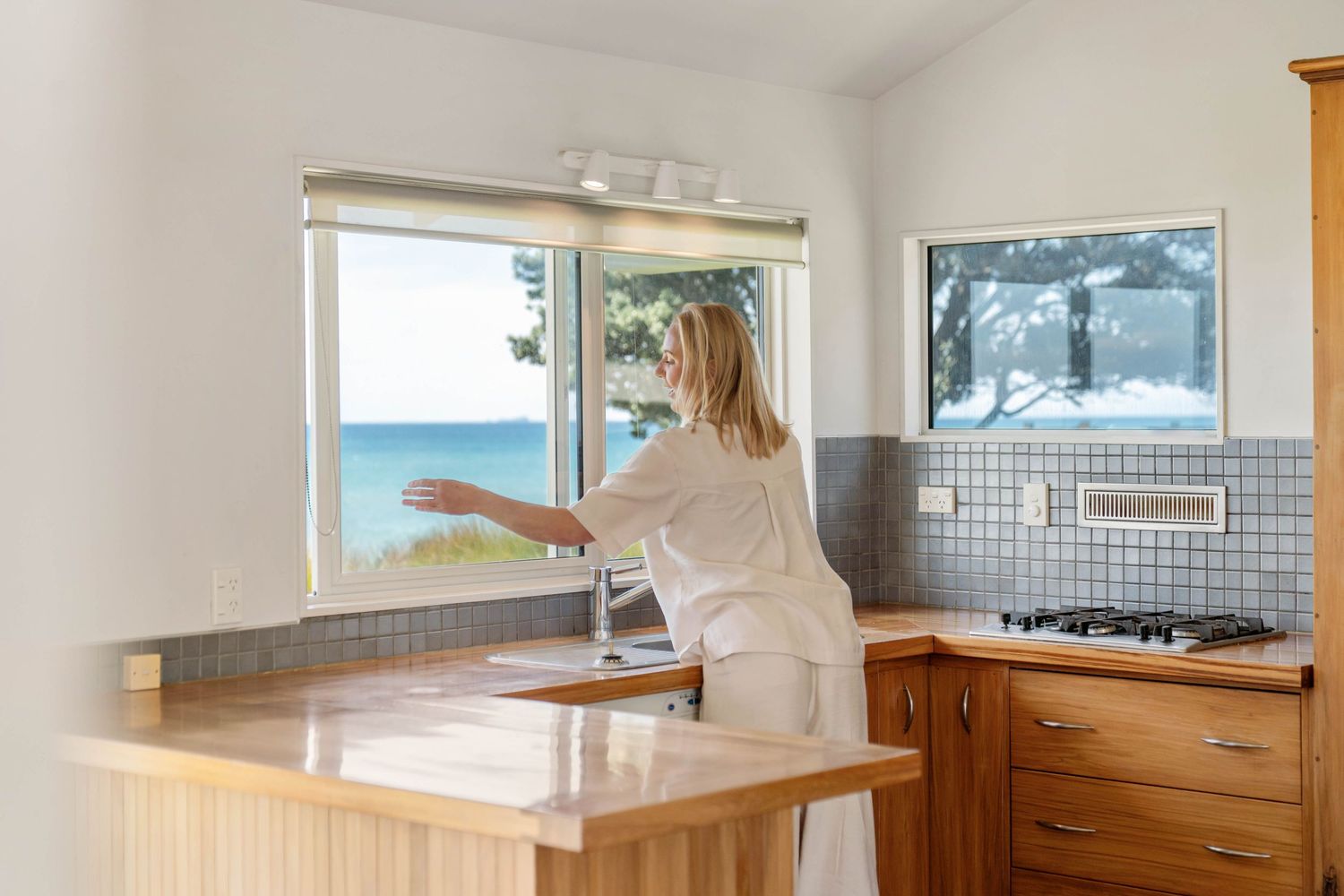 A bright kitchen interior with ocean views through a window and wooden cabinetry.