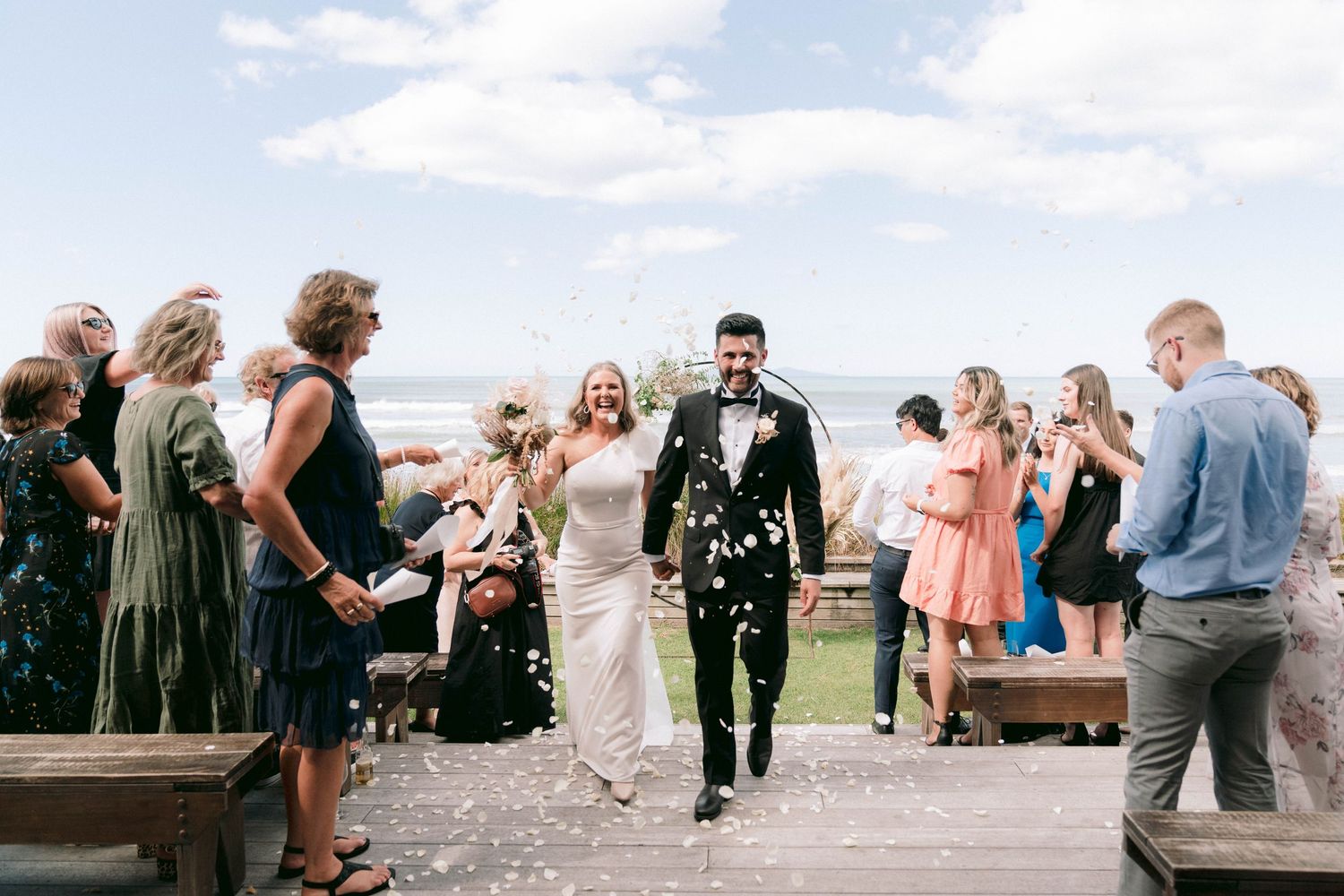 Wedding guests and celebrants gather outdoors for joyful reception celebration on sunny afternoon.