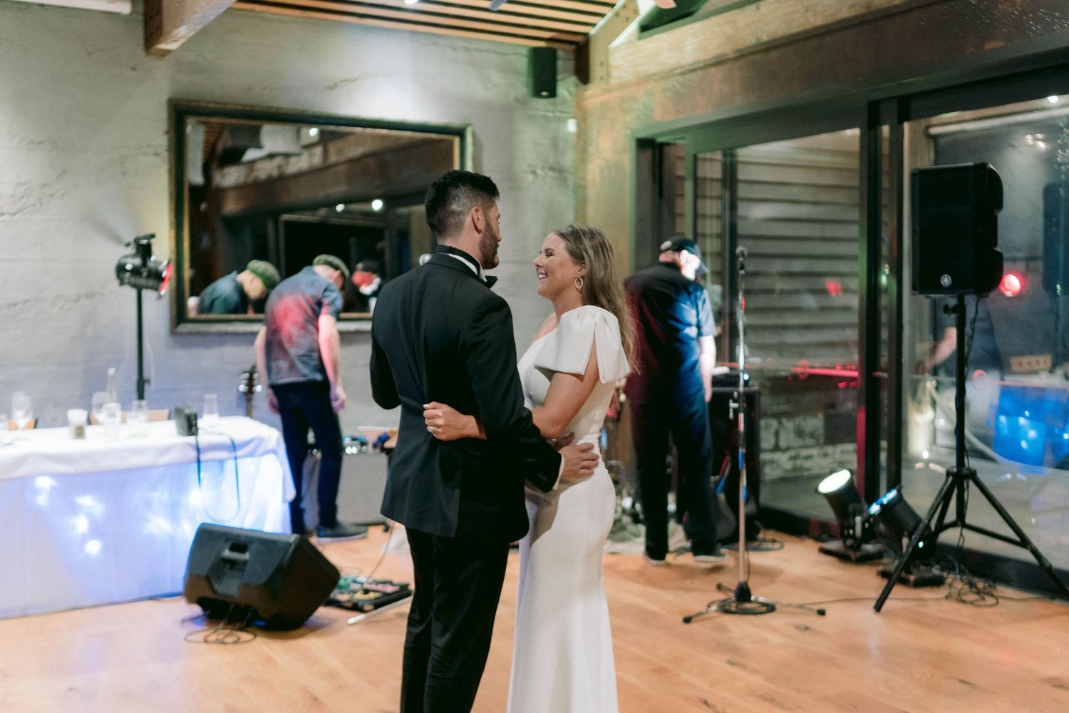 A romantic moment on the dance floor at an indoor wedding reception with lights and equipment visible.