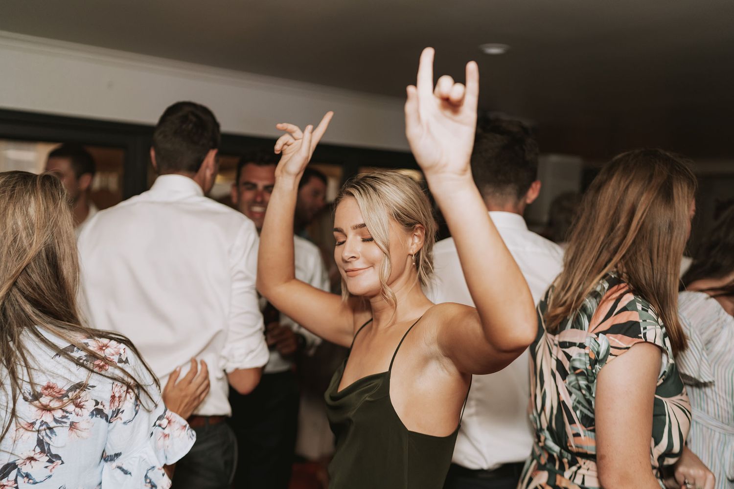 People dancing and celebrating at a party with raised hands in a dark indoor venue.