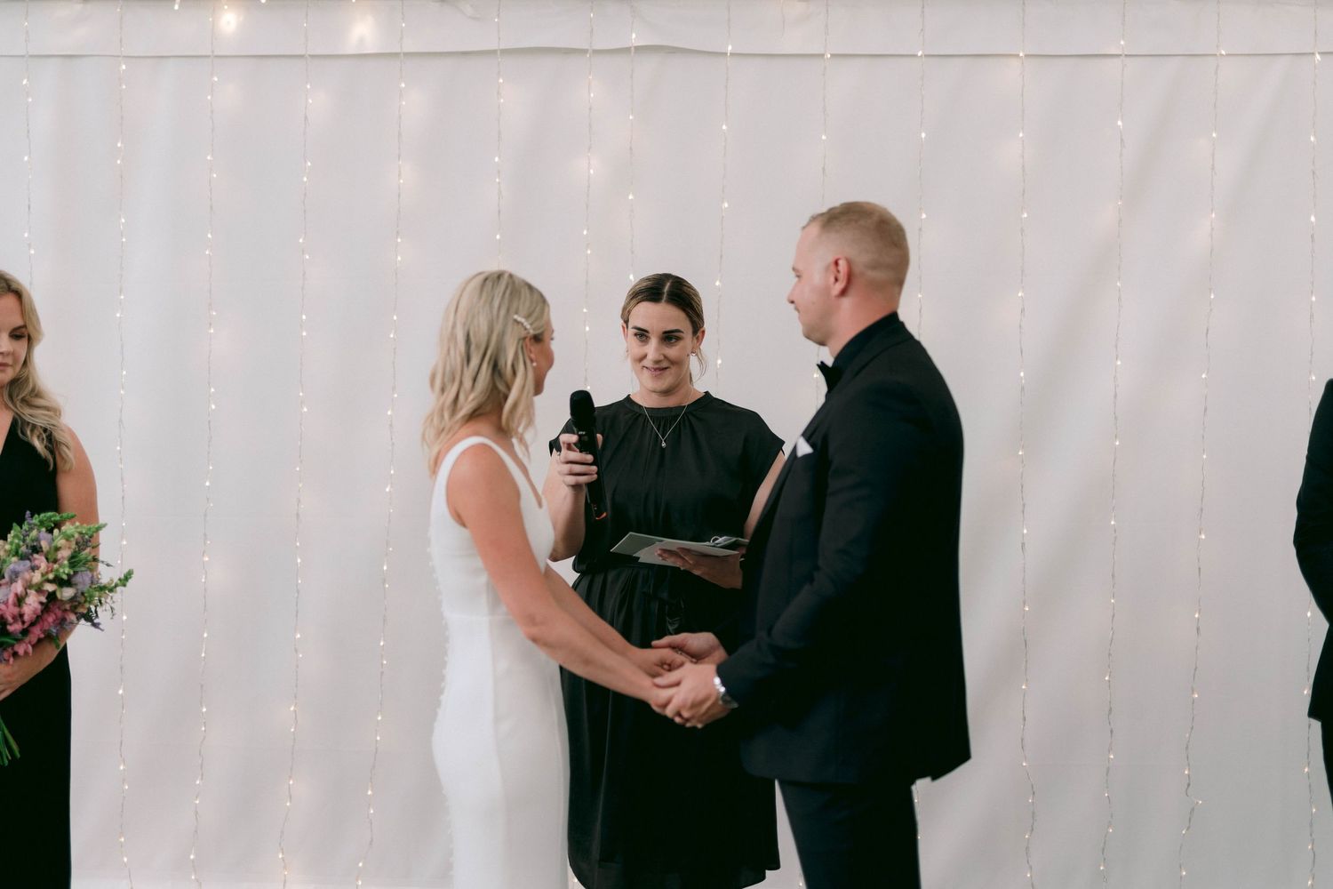 Guests at a wedding ceremony interacting and greeting each other in front of a white backdrop.