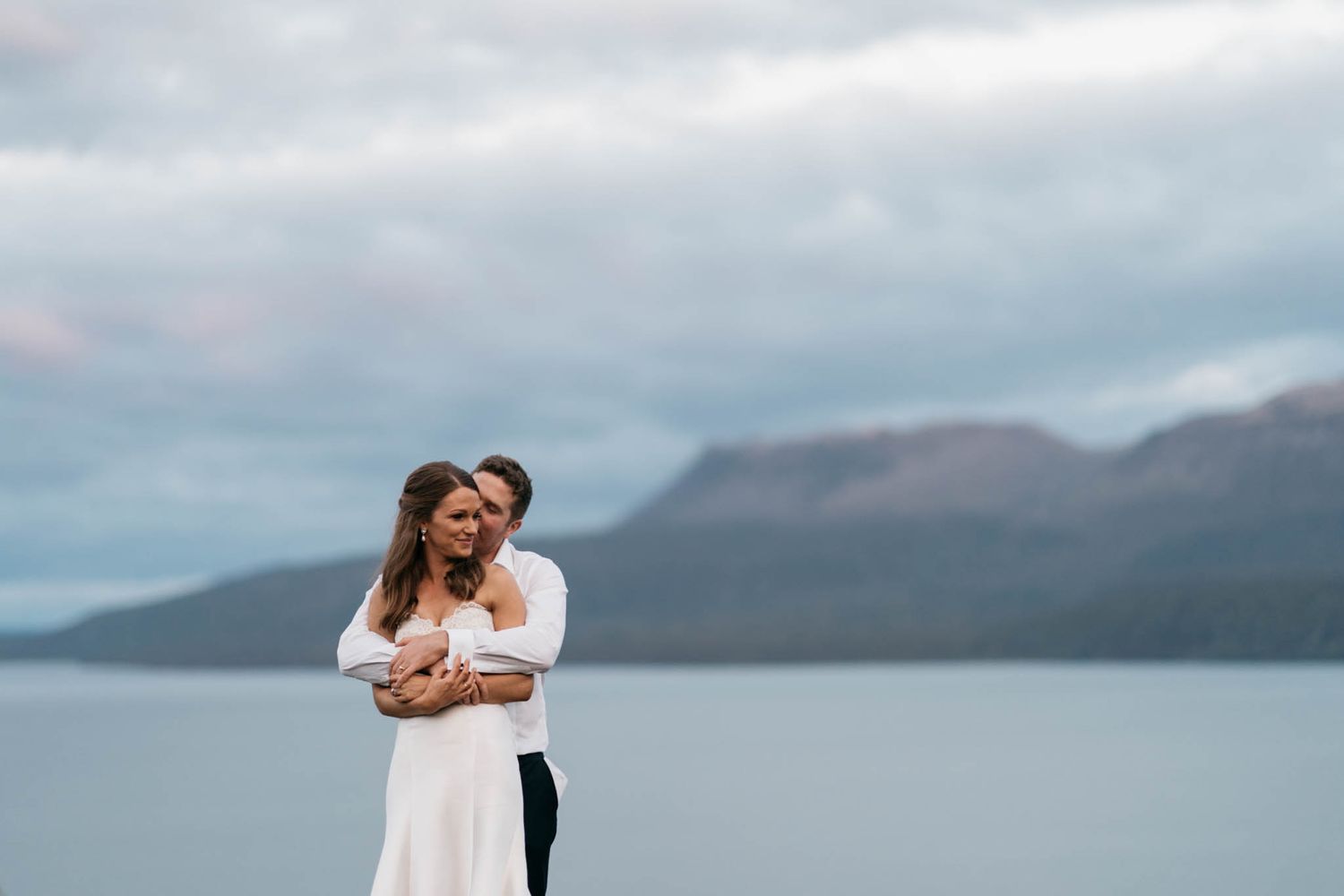 A couple embraces on a scenic overlook with misty mountains and a serene lake in the background.