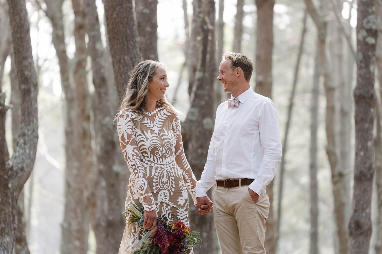 A romantic couple walks through a misty forest holding hands while wearing white lace and casual attire.