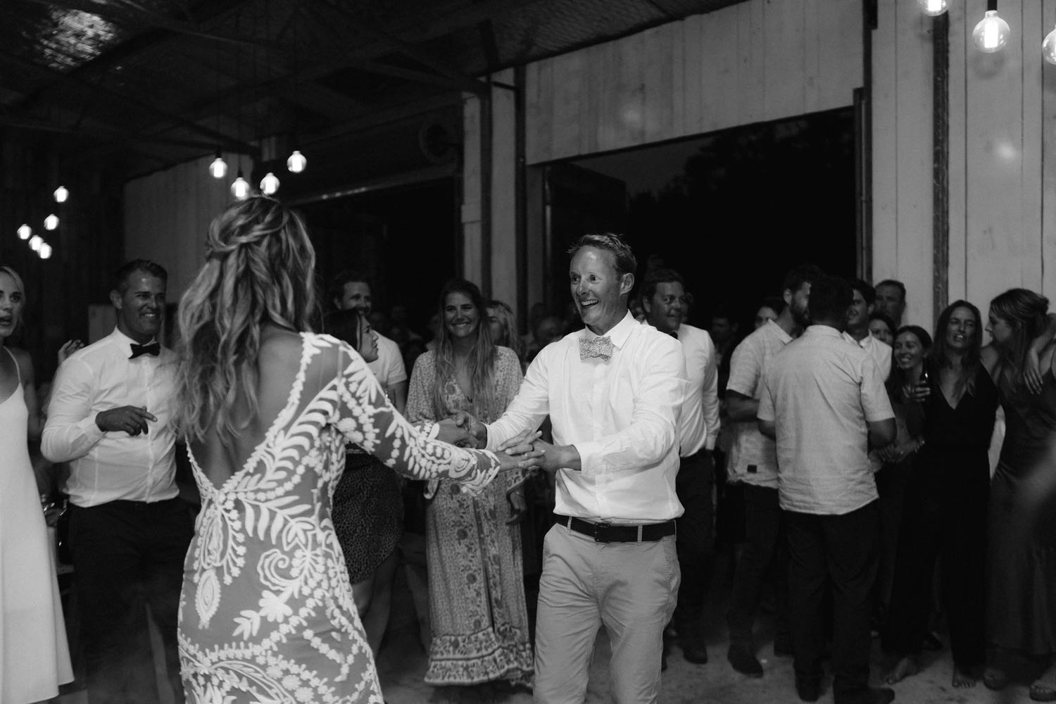People dancing at a reception venue with guests in background and festive lights creating a celebratory atmosphere.