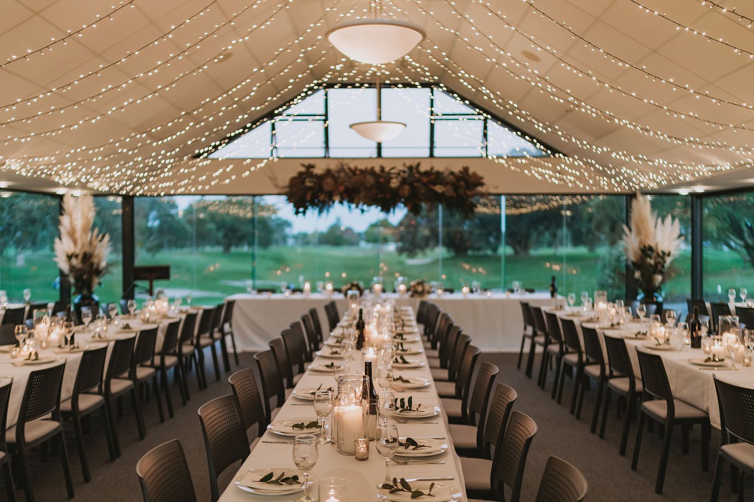 Long tables set for an elegant wedding reception under a tented pavilion with draped fabric ceiling and outdoor views.