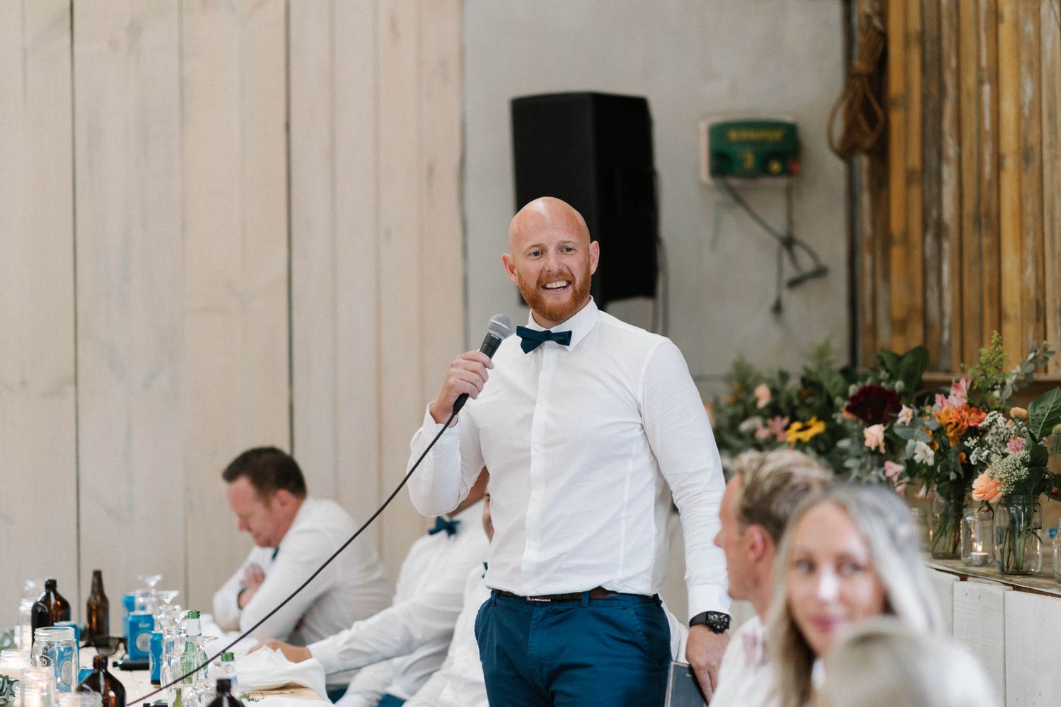 Guests and servers celebrating at an elegant indoor wedding reception with rustic wooden walls and floral centerpieces.