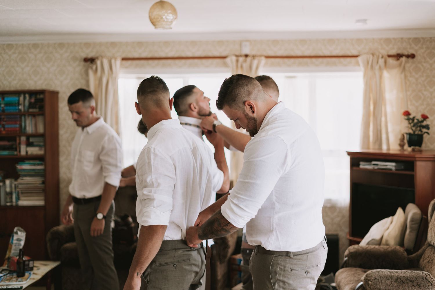 Panoramic view of groomsmen getting ready in formal attire for a wedding ceremony in a traditional indoor setting.