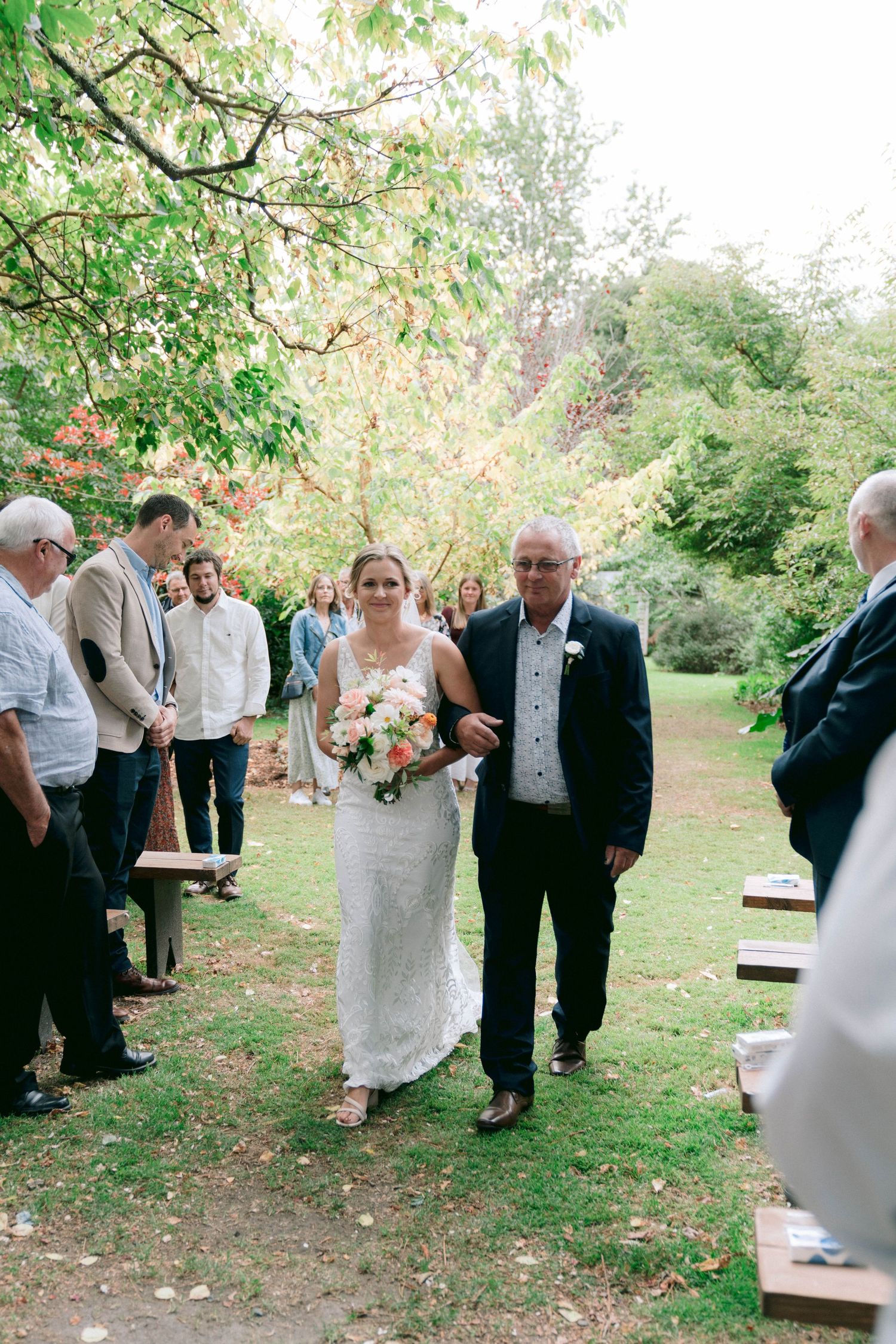 Wedding ceremony processional on a garden path surrounded by lush greenery.
