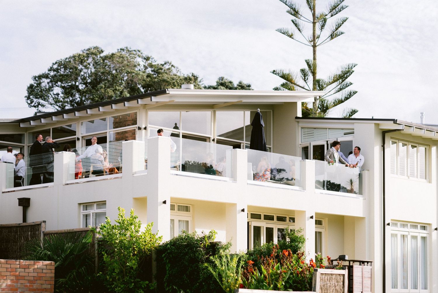 Modern white two-story beach house with balconies and tropical landscaping.