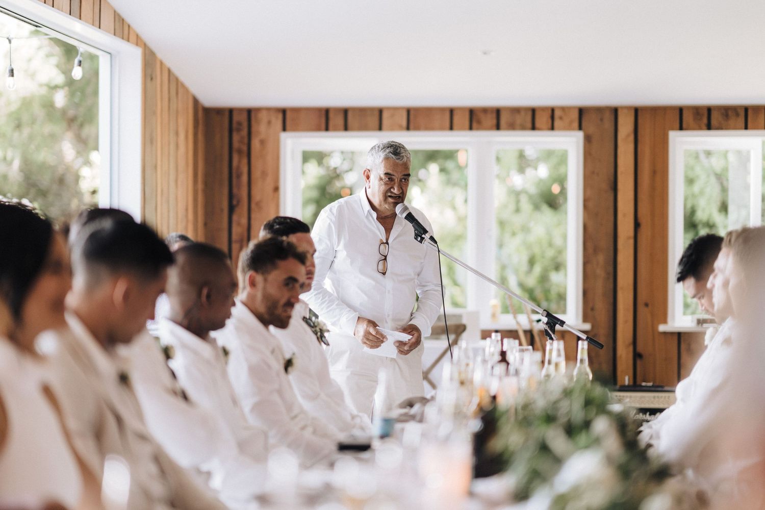 Wedding party dressed in crisp white attire lined up in a wood-paneled room.