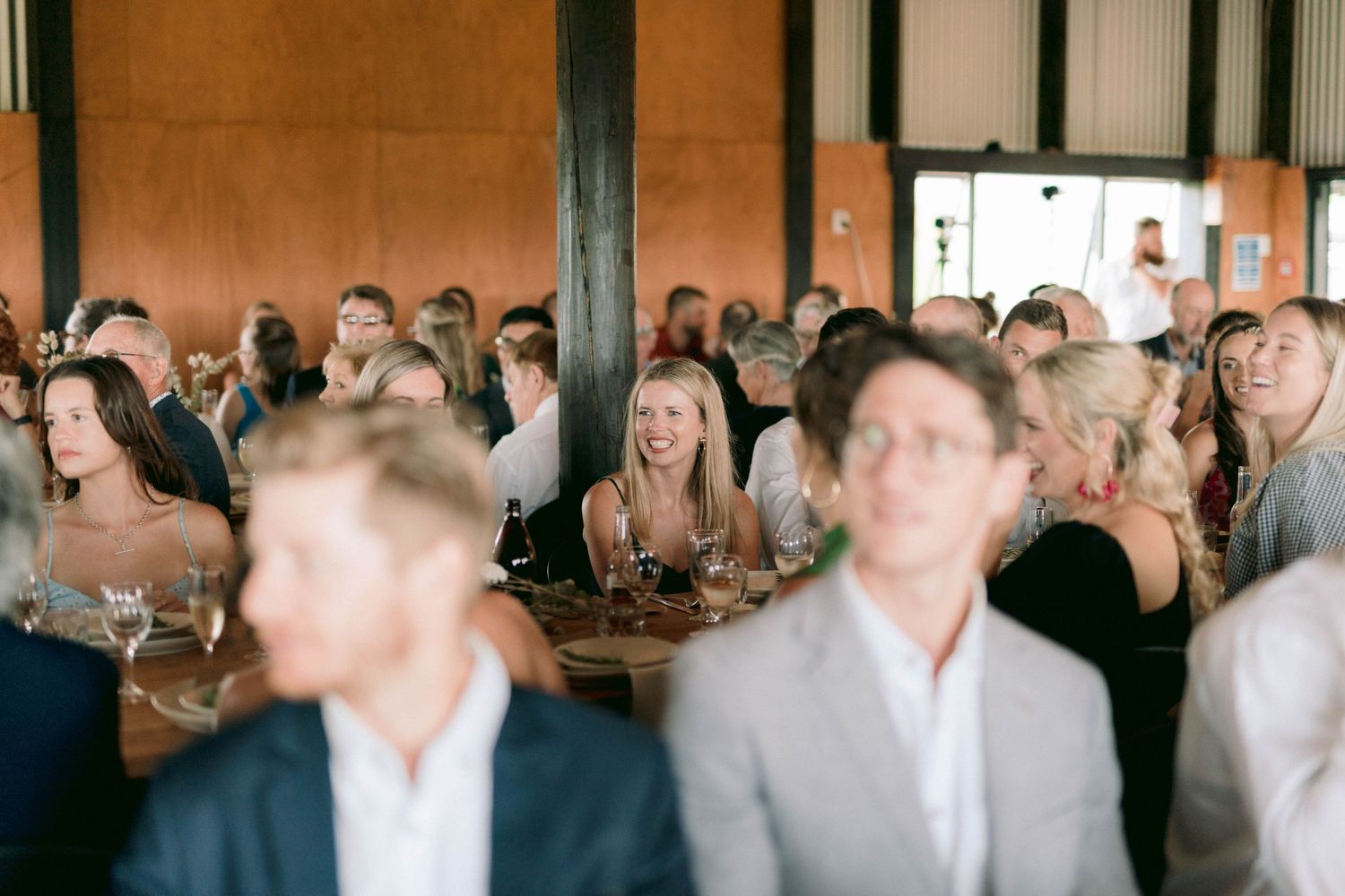 Wedding reception guests mingling in a rustic indoor venue with wooden beams.