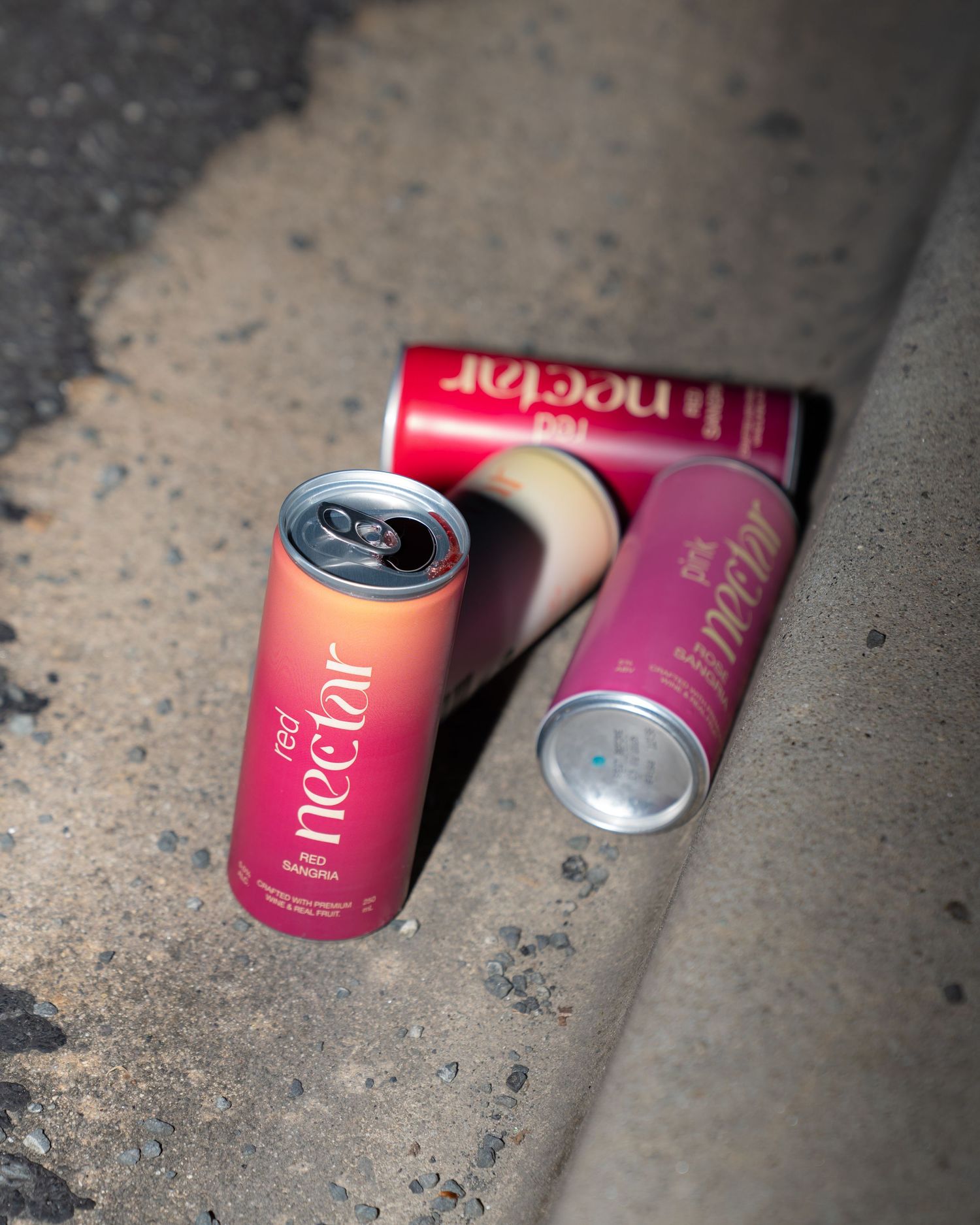 Two pink Nectar drink cans lying on concrete surface with dramatic lighting.