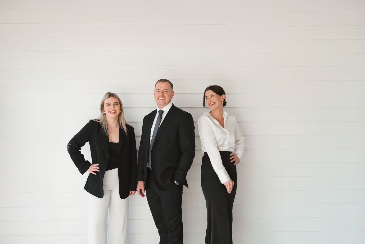 Three business professionals in black and white attire posing together against a white wall.