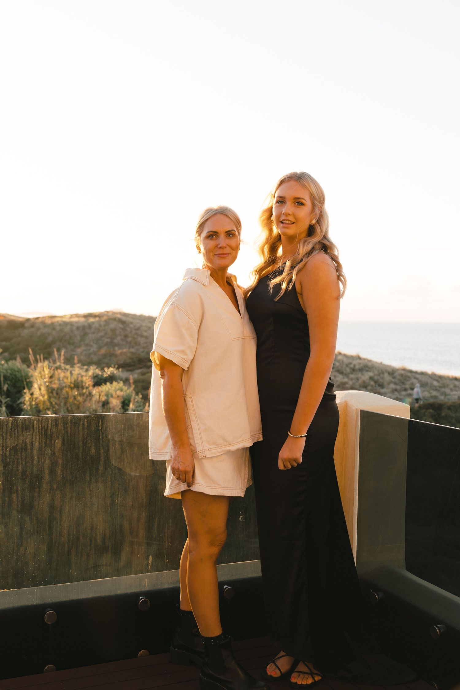 Couple stands together on outdoor terrace during golden hour sunset against mountain backdrop.