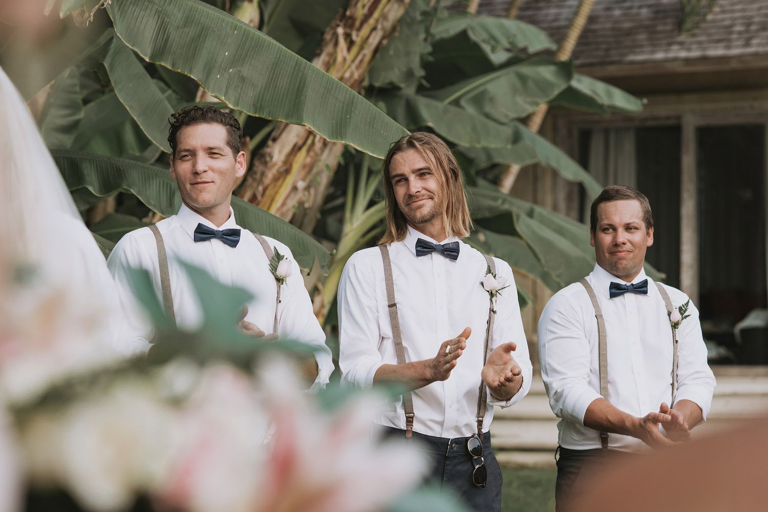 Groomsmen in white shirts, suspenders and bow ties at tropical wedding venue.