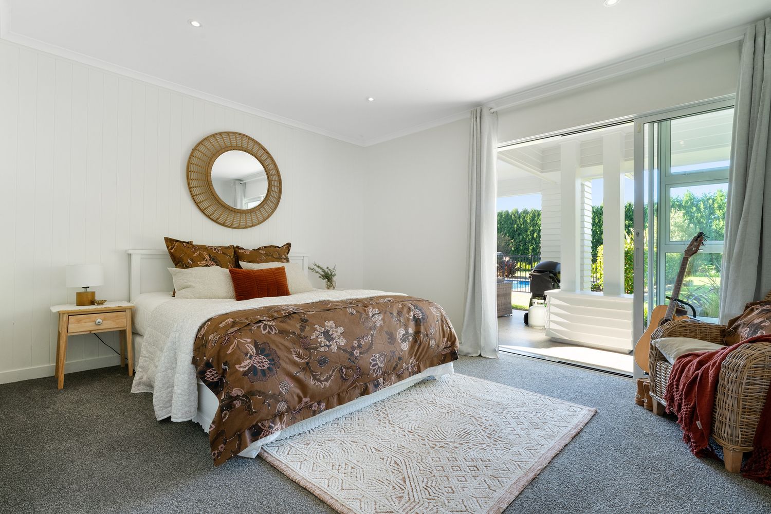 Spacious master bedroom with sliding doors to patio, round gold mirror, and brown bedding accents.