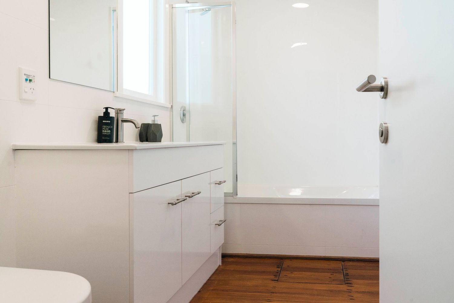 Clean white bathroom interior with wooden floor, modern vanity, and minimalist fixtures.