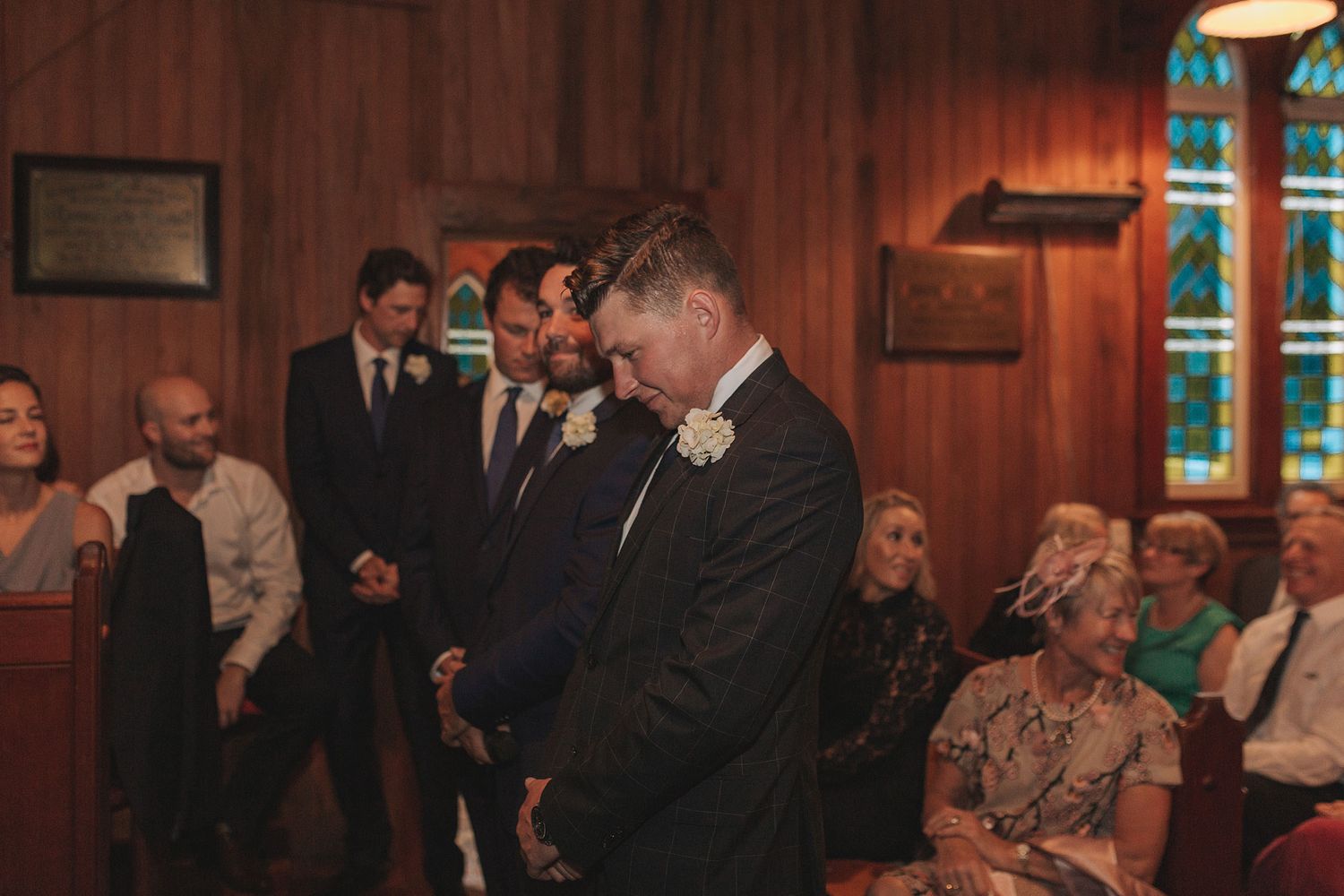 People dancing and socializing at an indoor party or celebration with warm wood-paneled walls and dim lighting.