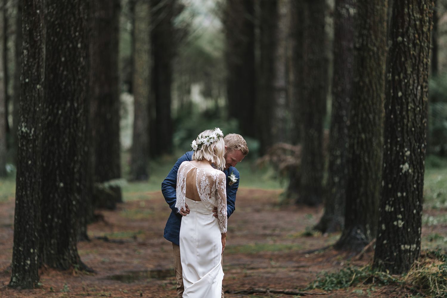 Couple holding hands while walking down a forested path lined with tall pine trees.