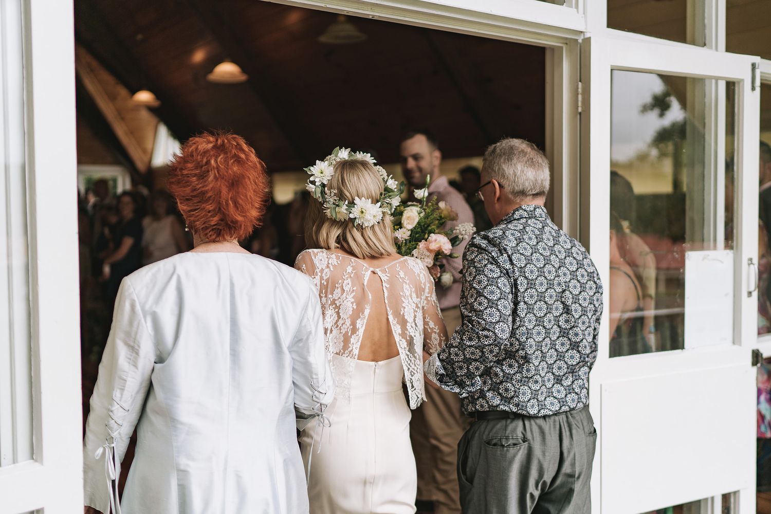 A wedding celebration scene through open french doors with guests in formal attire gathering inside a bright venue.