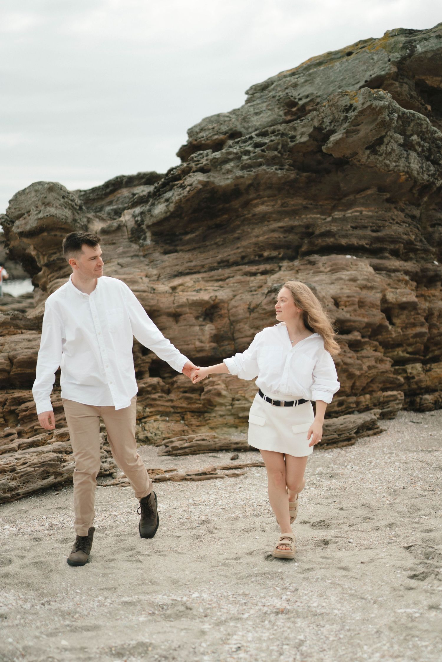 Joyful couple running and playing along rocky coastline in matching outfits.