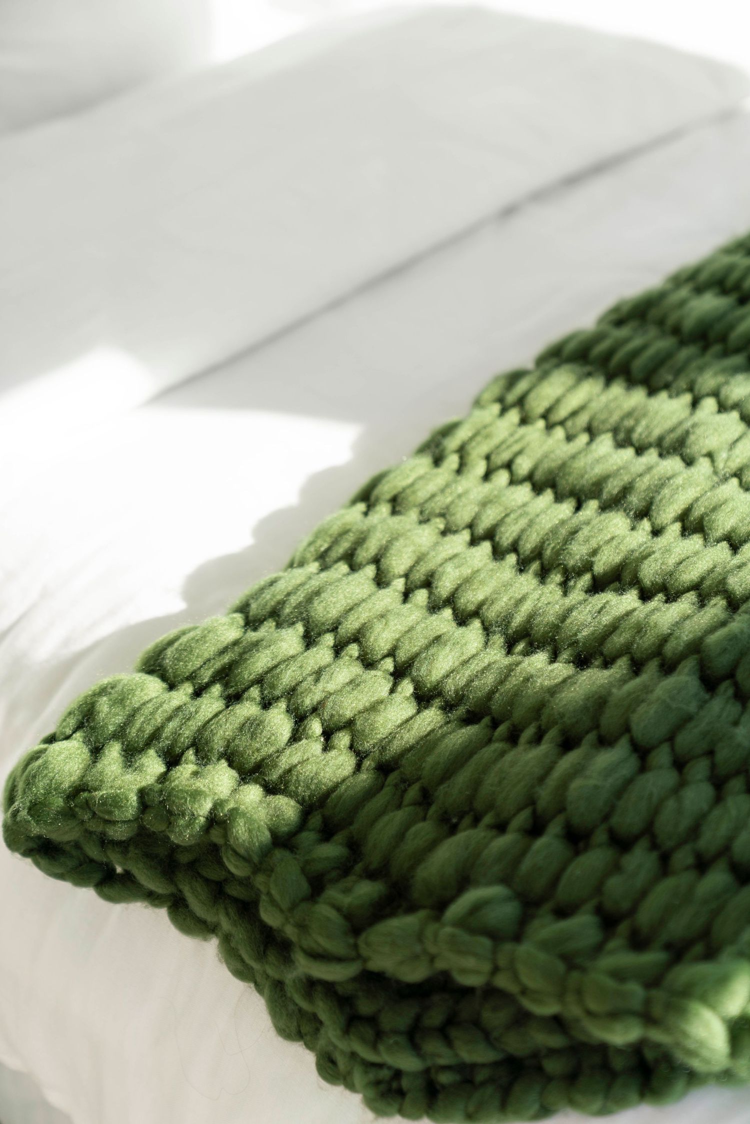 Close-up of chunky knit green throw blanket with textured pattern in natural light.