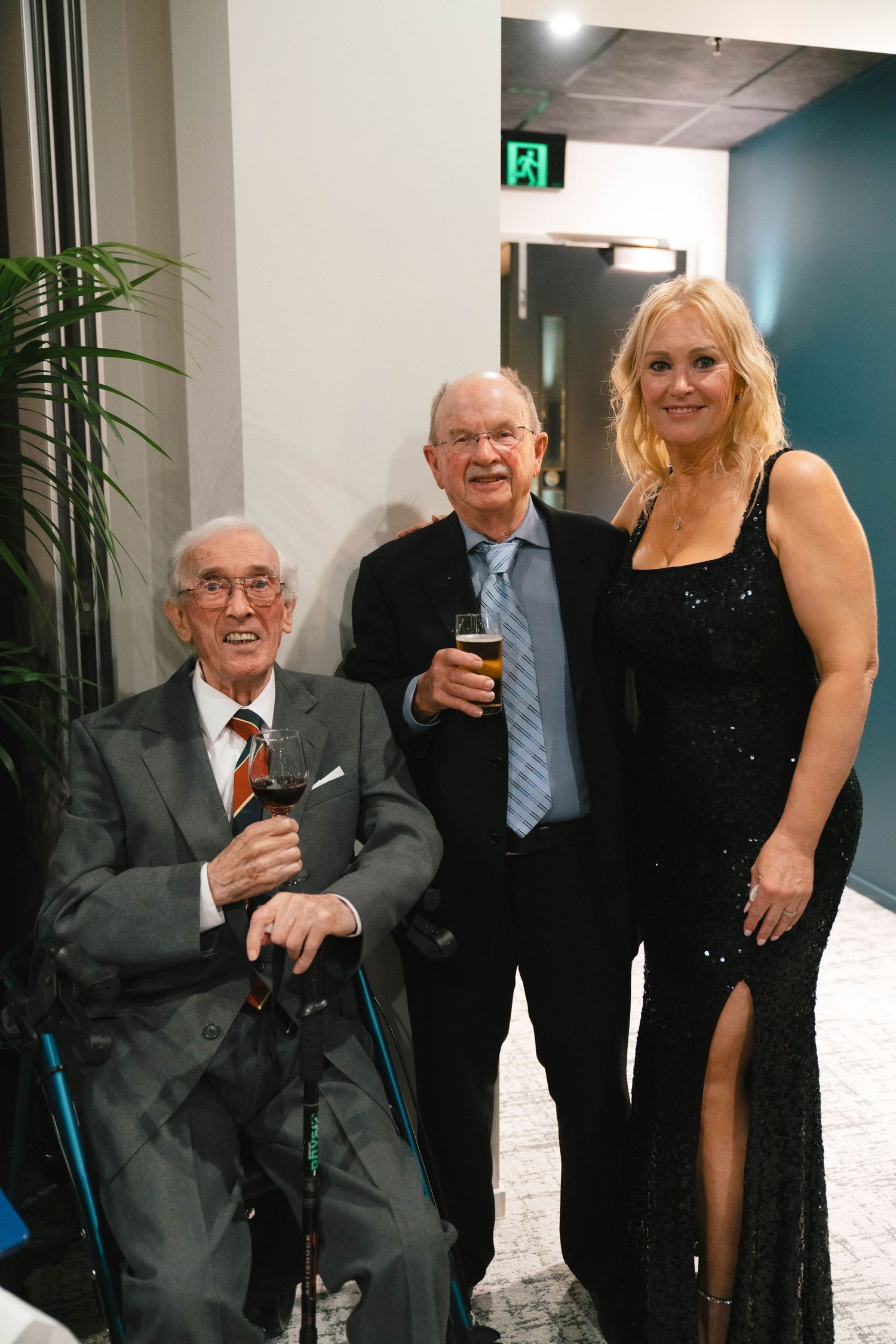 Guests in formal attire gathering near modern indoor decor with exit sign visible.