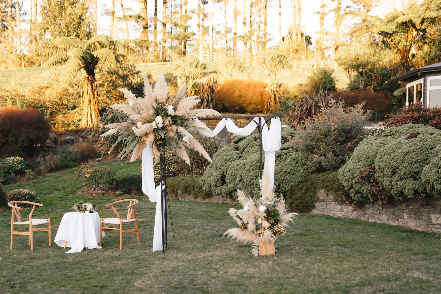 An outdoor wedding ceremony setup at sunset with white pillars and floral arrangements creating a romantic atmosphere.