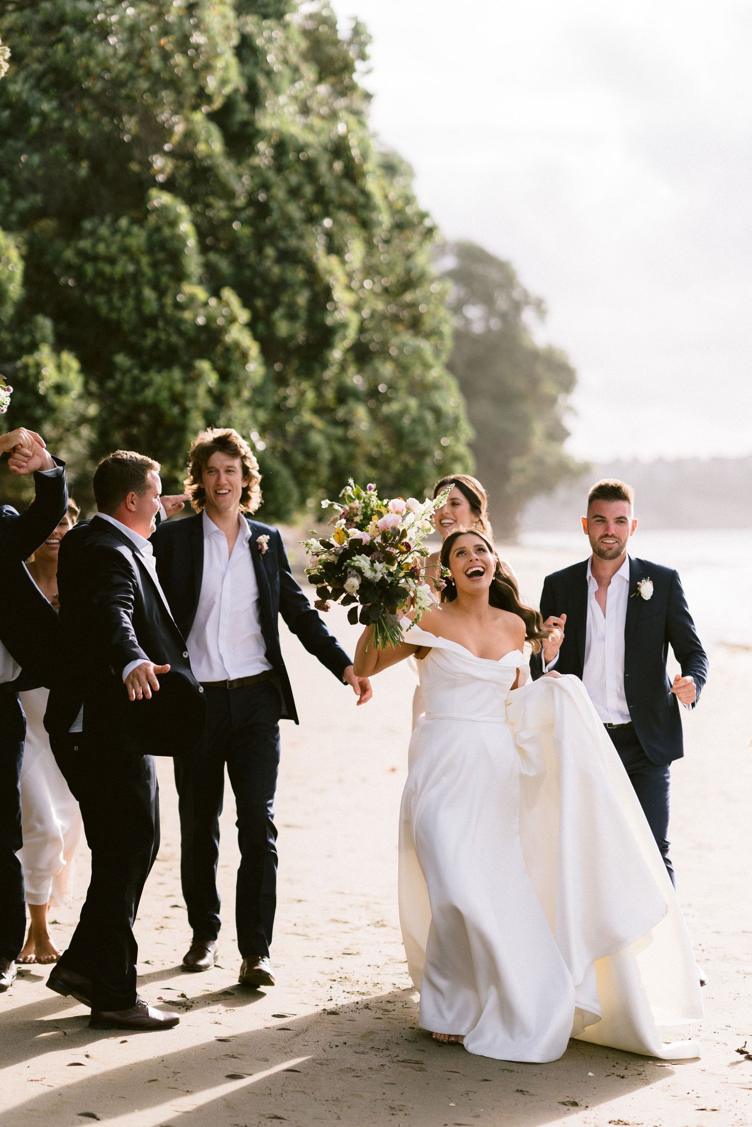 Wedding party walking and laughing together along scenic beach shoreline.
