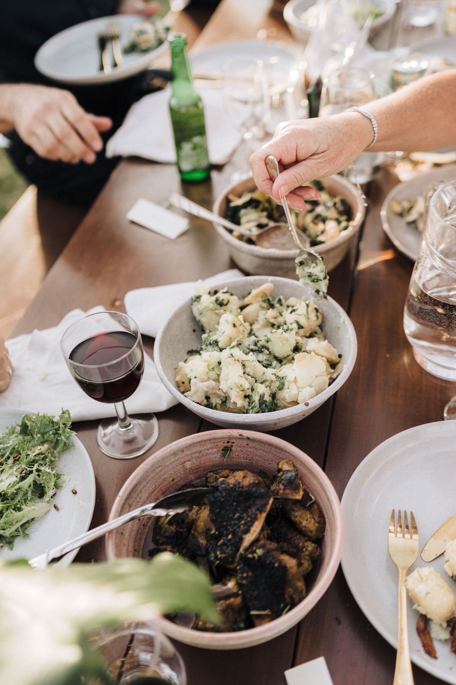Family-style dining table set with shared plates of food, wine glasses, and casual dinner settings.