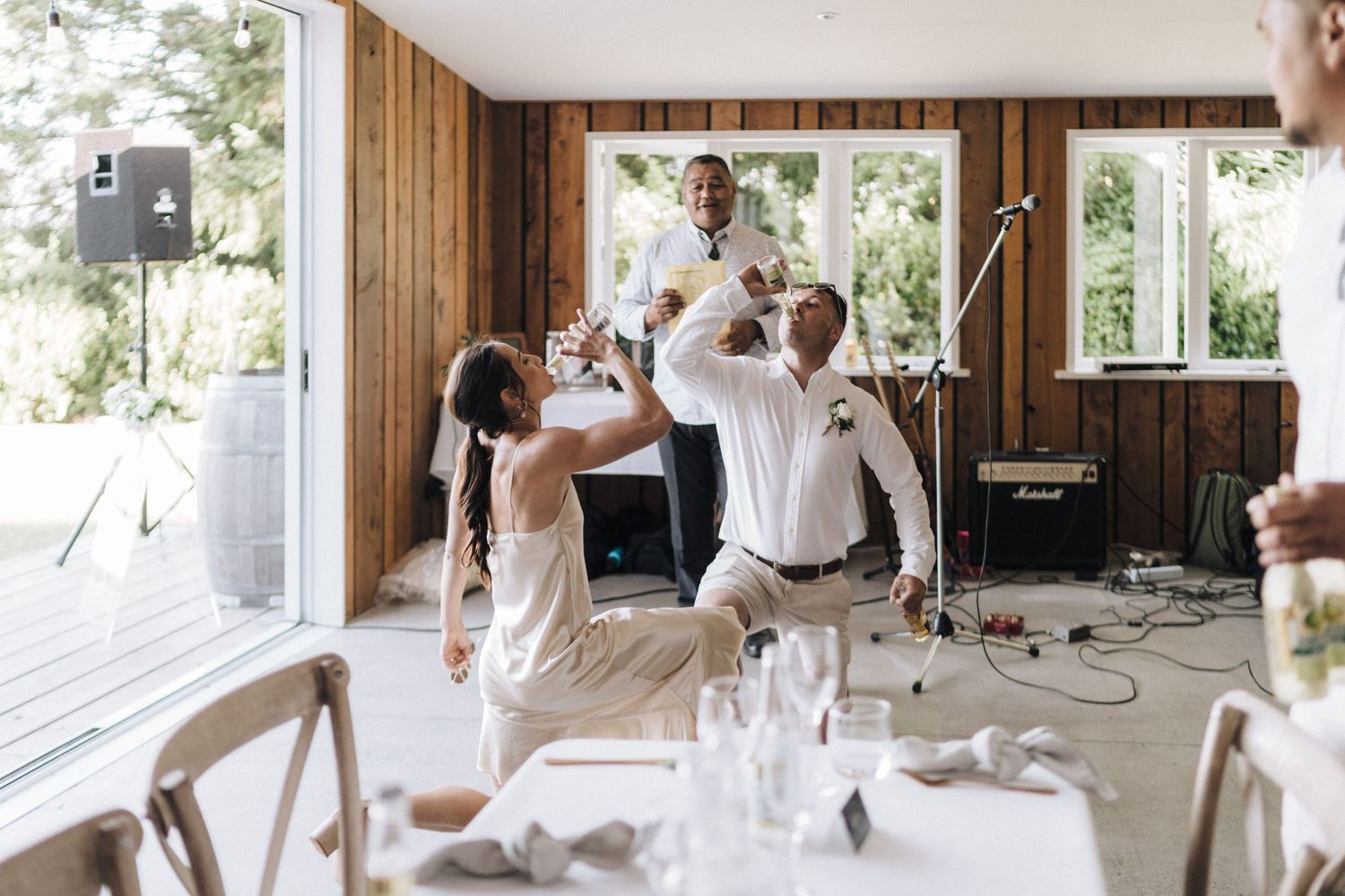 Wedding guests dance and celebrate energetically in a wood-paneled reception room.