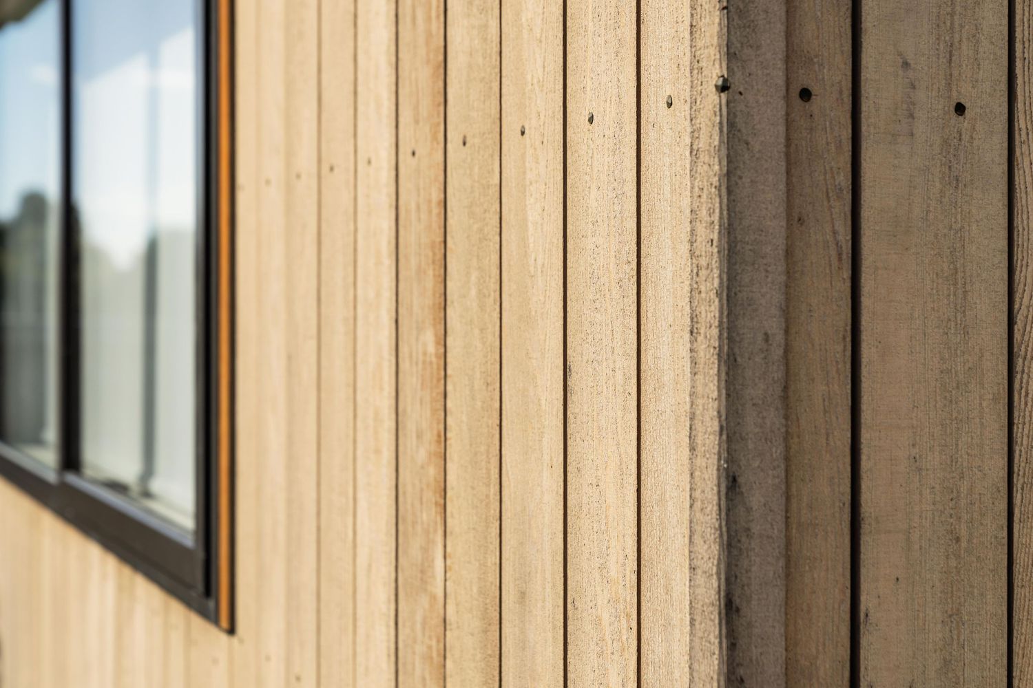 Close-up view of natural wood siding on a building exterior with a window edge visible in the frame.
