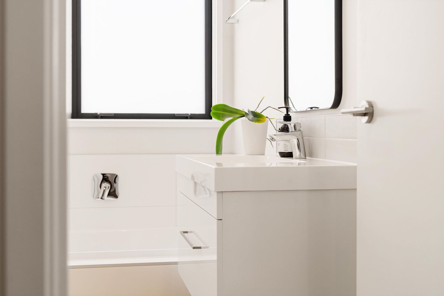 Modern white bathroom interior with minimalist sink, fixtures, and natural light through window.