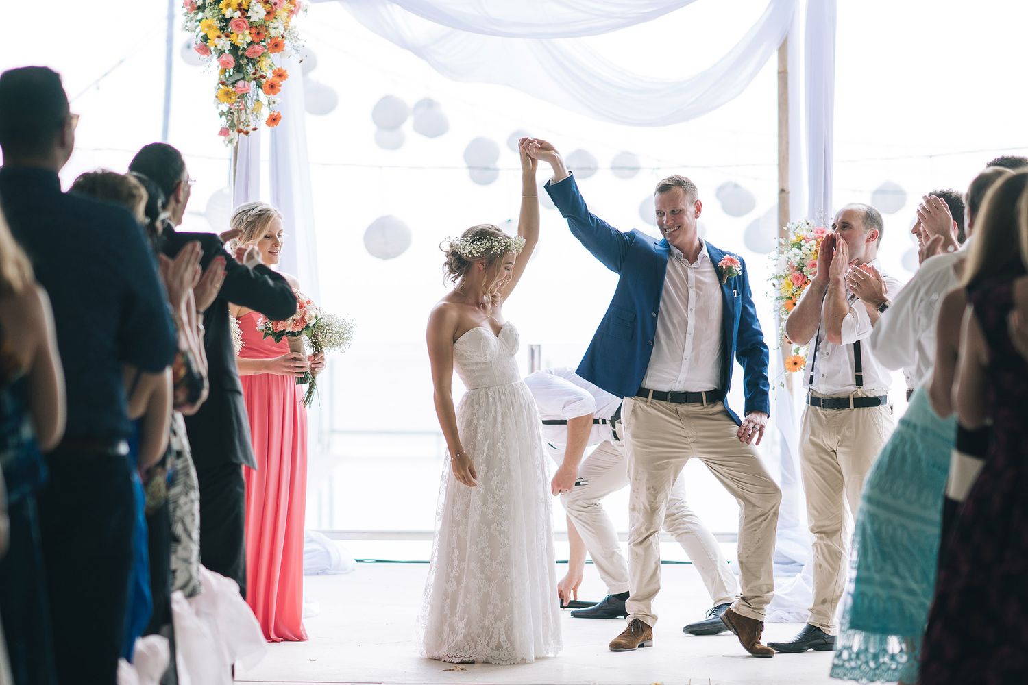 Wedding couple celebrating and dancing with guests under a white canopy during daytime celebration.