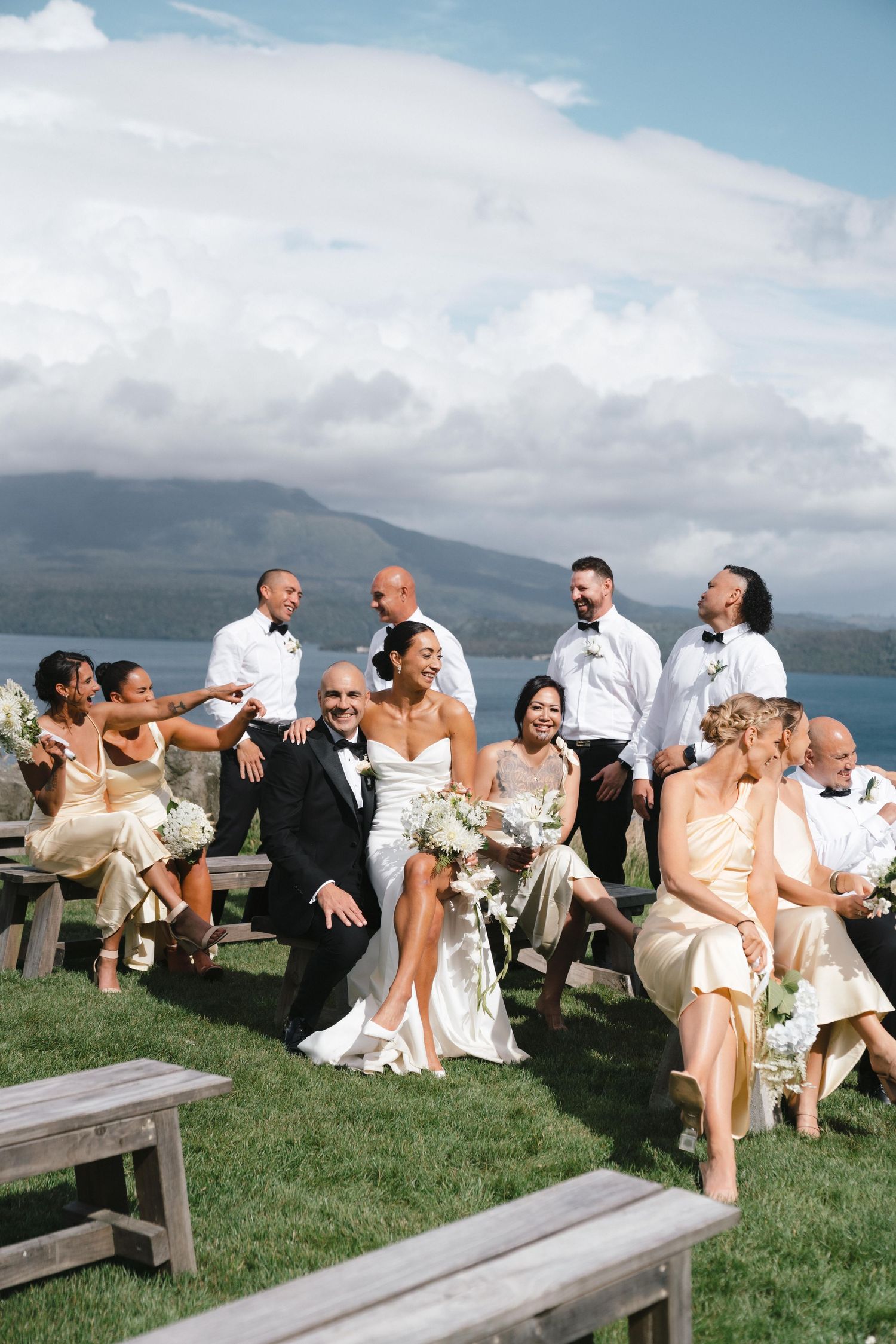 Wedding party and guests gathered on wooden benches enjoying a casual outdoor celebration with mountain views.