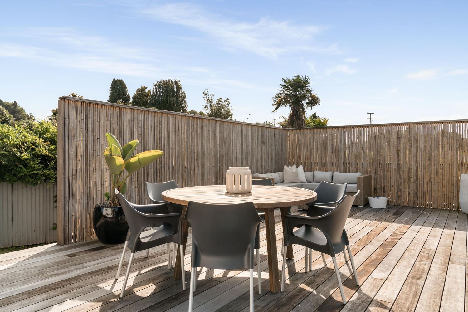 Modern outdoor wooden deck with round dining table and black chairs surrounded by privacy fencing.