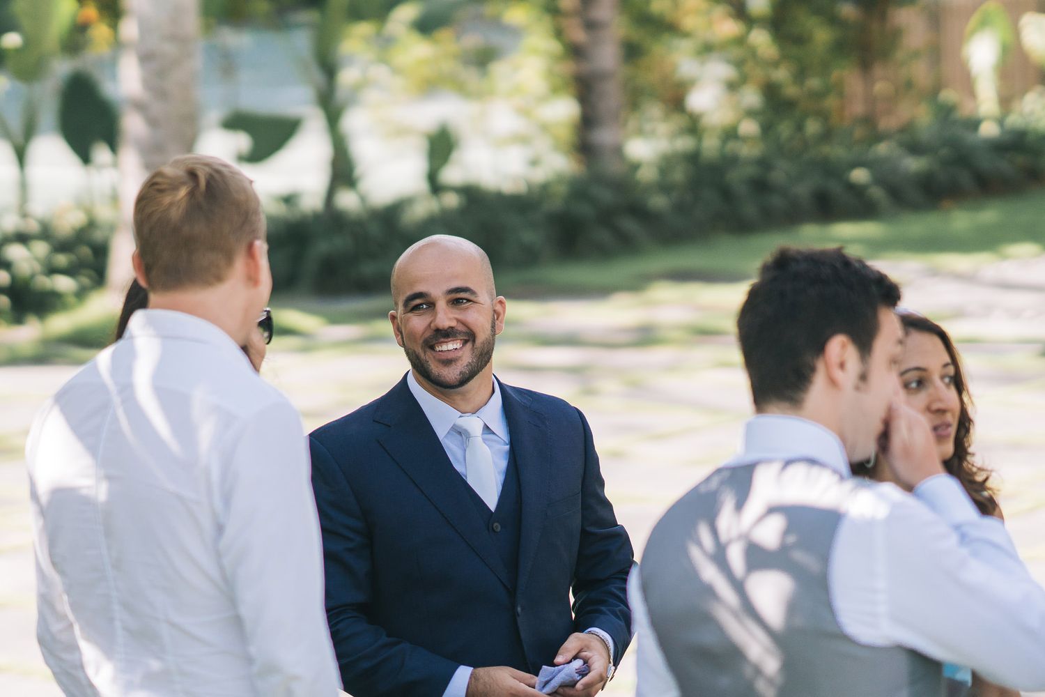 People in formal attire interacting outdoors during a sunny daytime event.