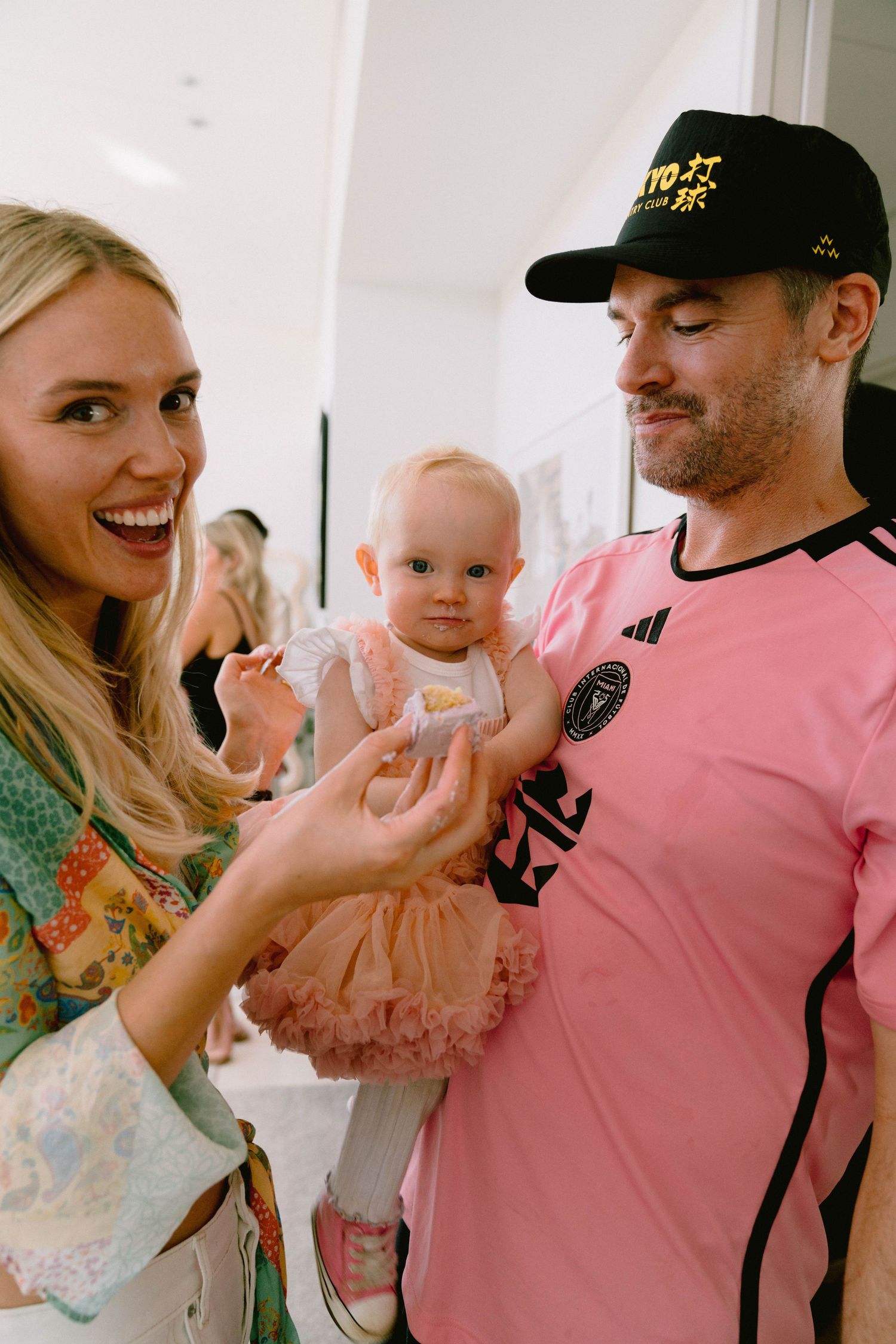 A baby in a pink tulle dress being held while others smile and interact.