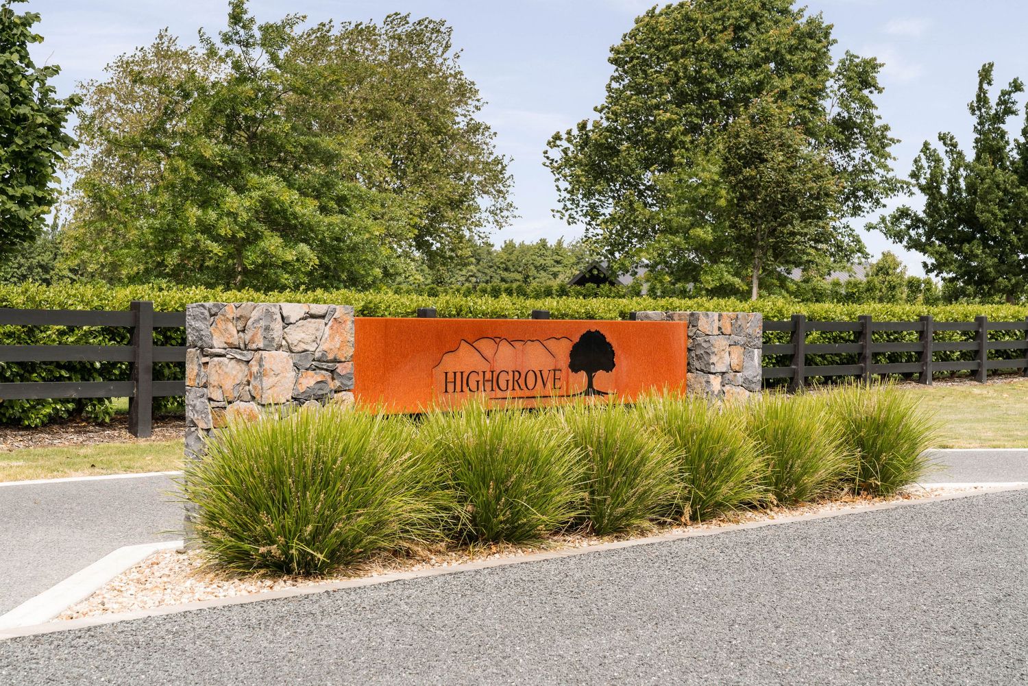 Orange and stone entrance monument with black tree logo and decorative grasses.
