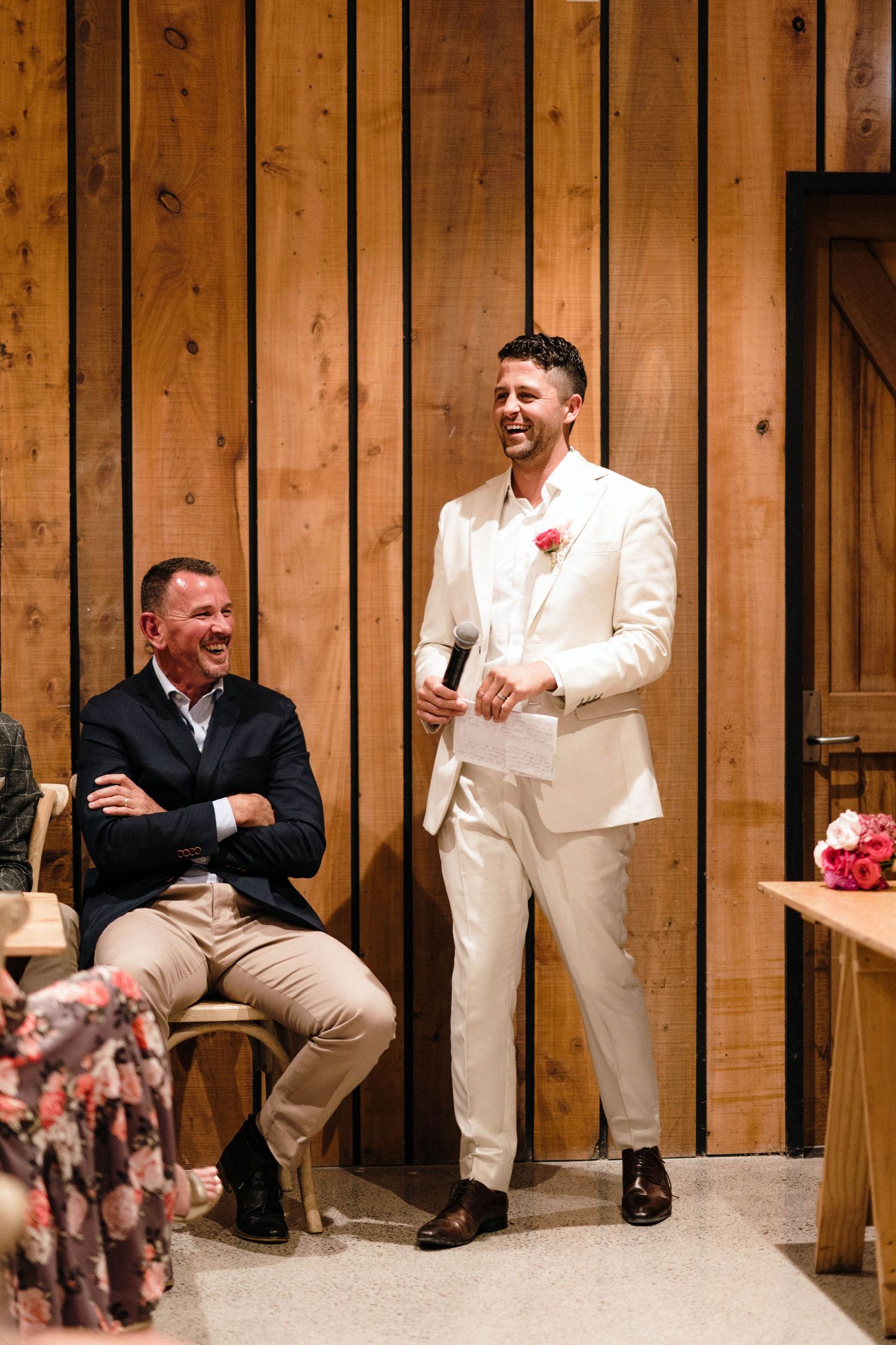 Groomsmen in cream suits laughing together against wooden paneled walls.