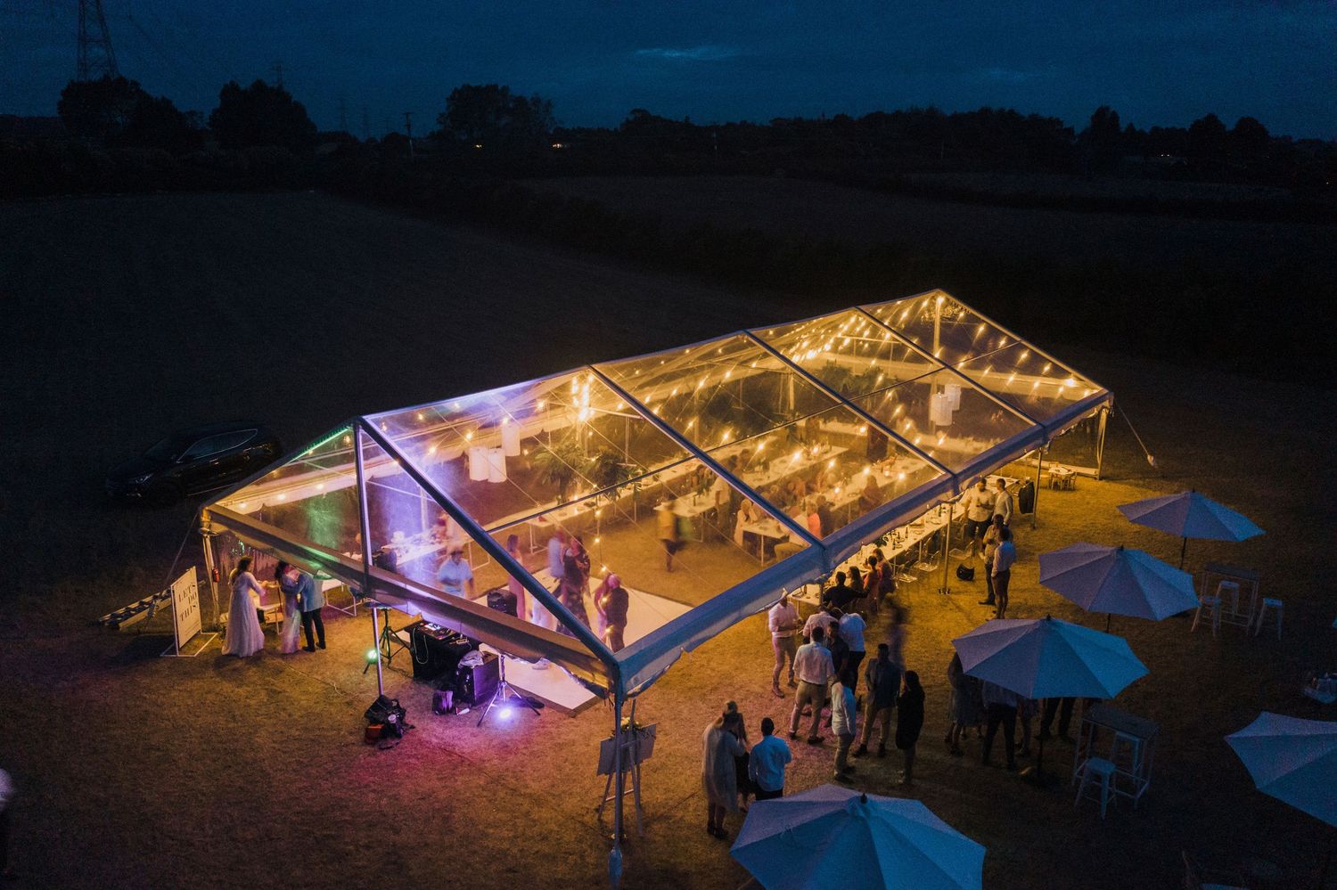 Illuminated outdoor wedding reception tents glowing against the dark night sky.