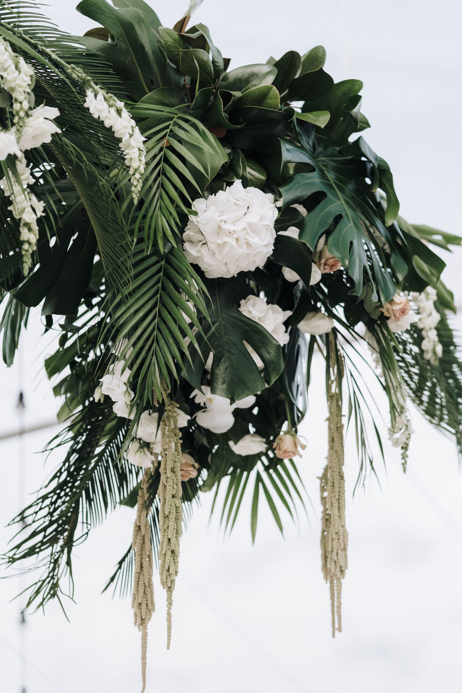 Tropical wedding decor featuring lush palm leaves and white flowers hanging from the ceiling.