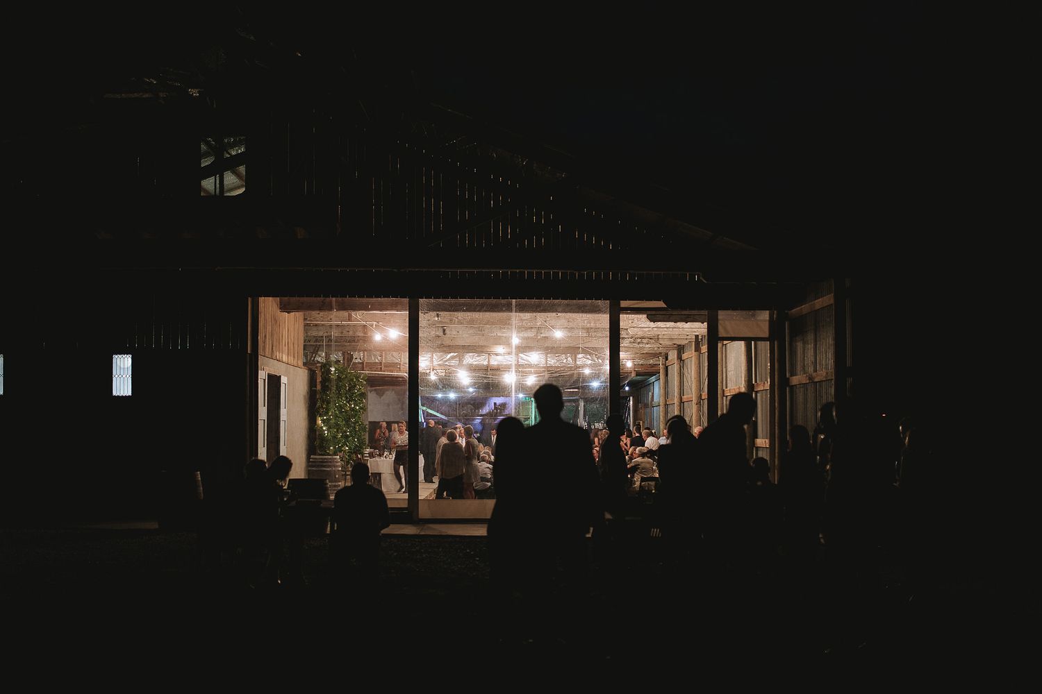 A dimly lit storefront glows at night with silhouettes of people visible through the illuminated windows.