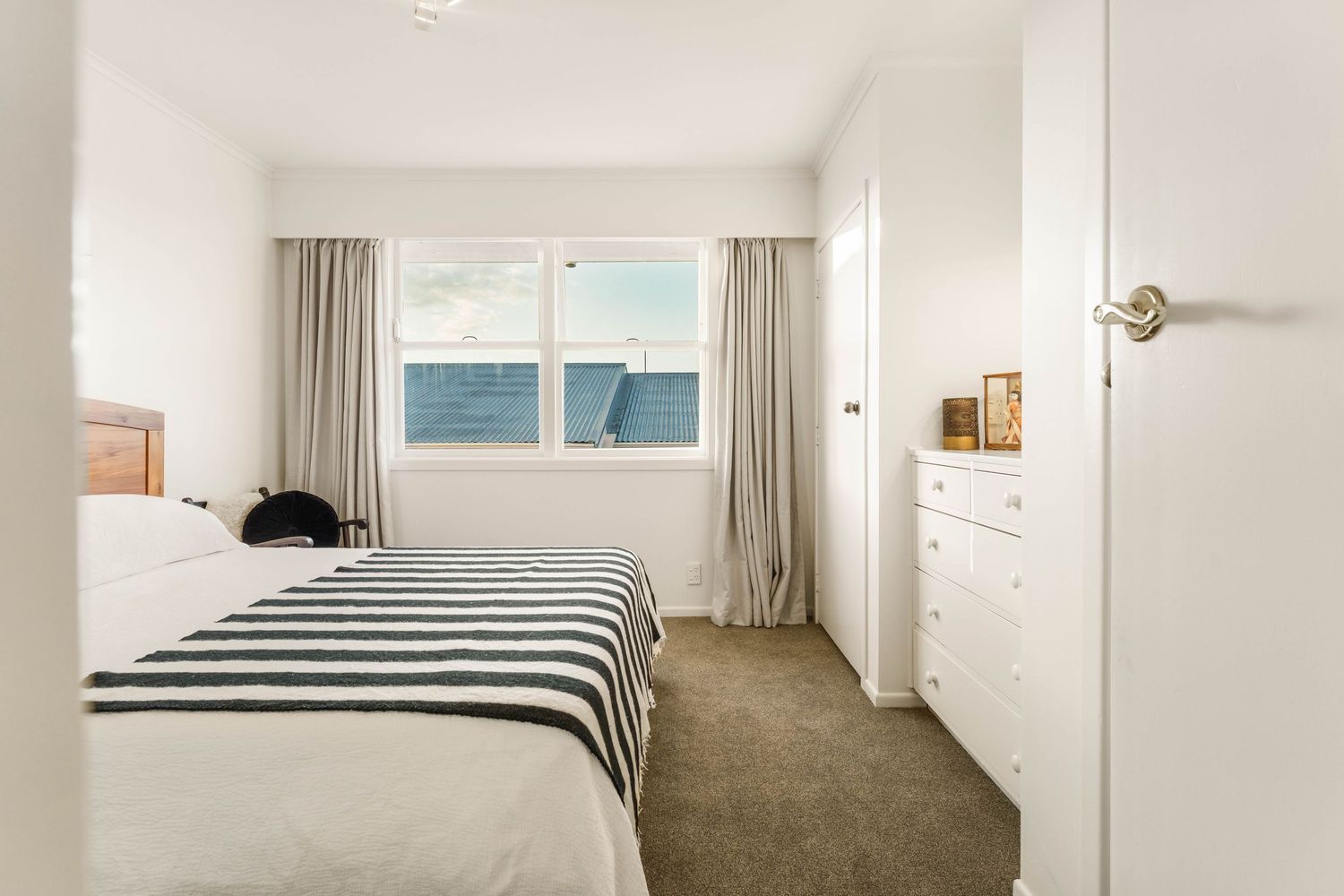 Minimalist white bedroom interior with natural light streaming through large windows.