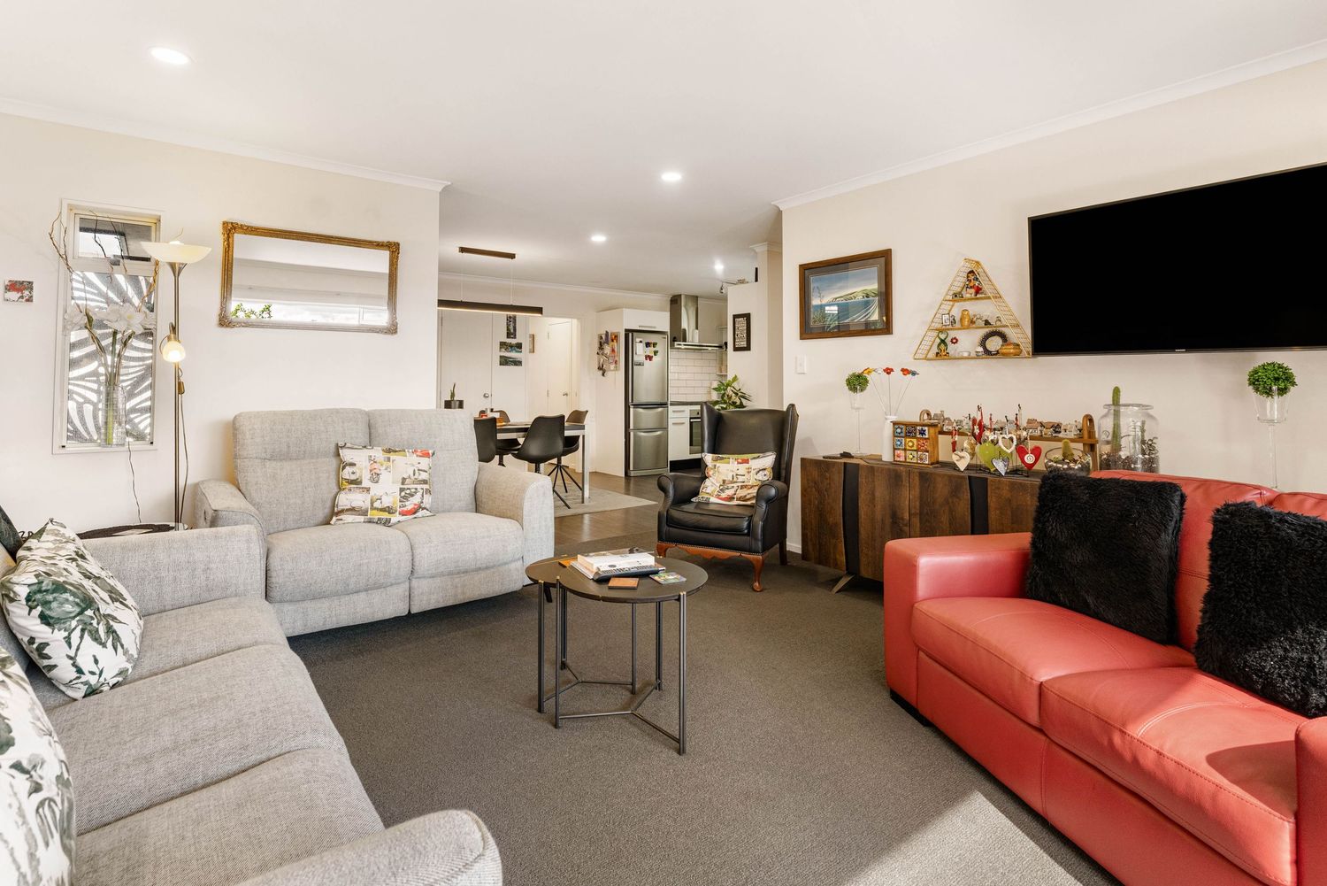 Spacious living room with grey couch, red accent sofa, and modern decor under recessed lighting.