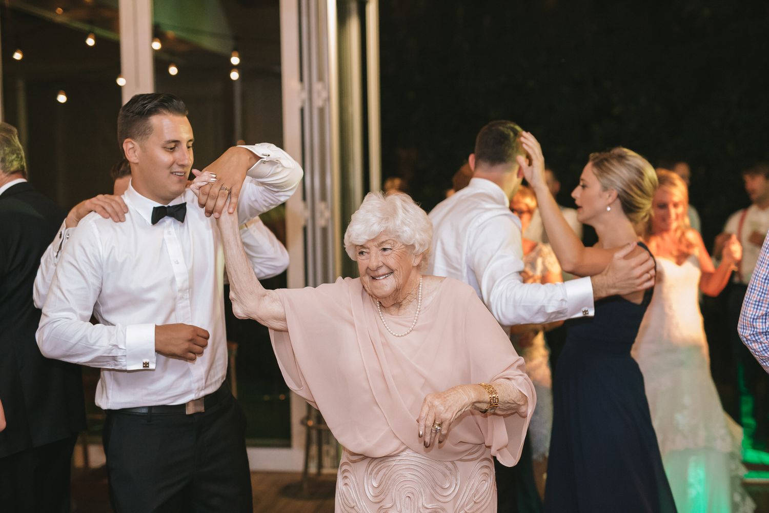 People dancing and celebrating at an elegant wedding reception with dim warm lighting.